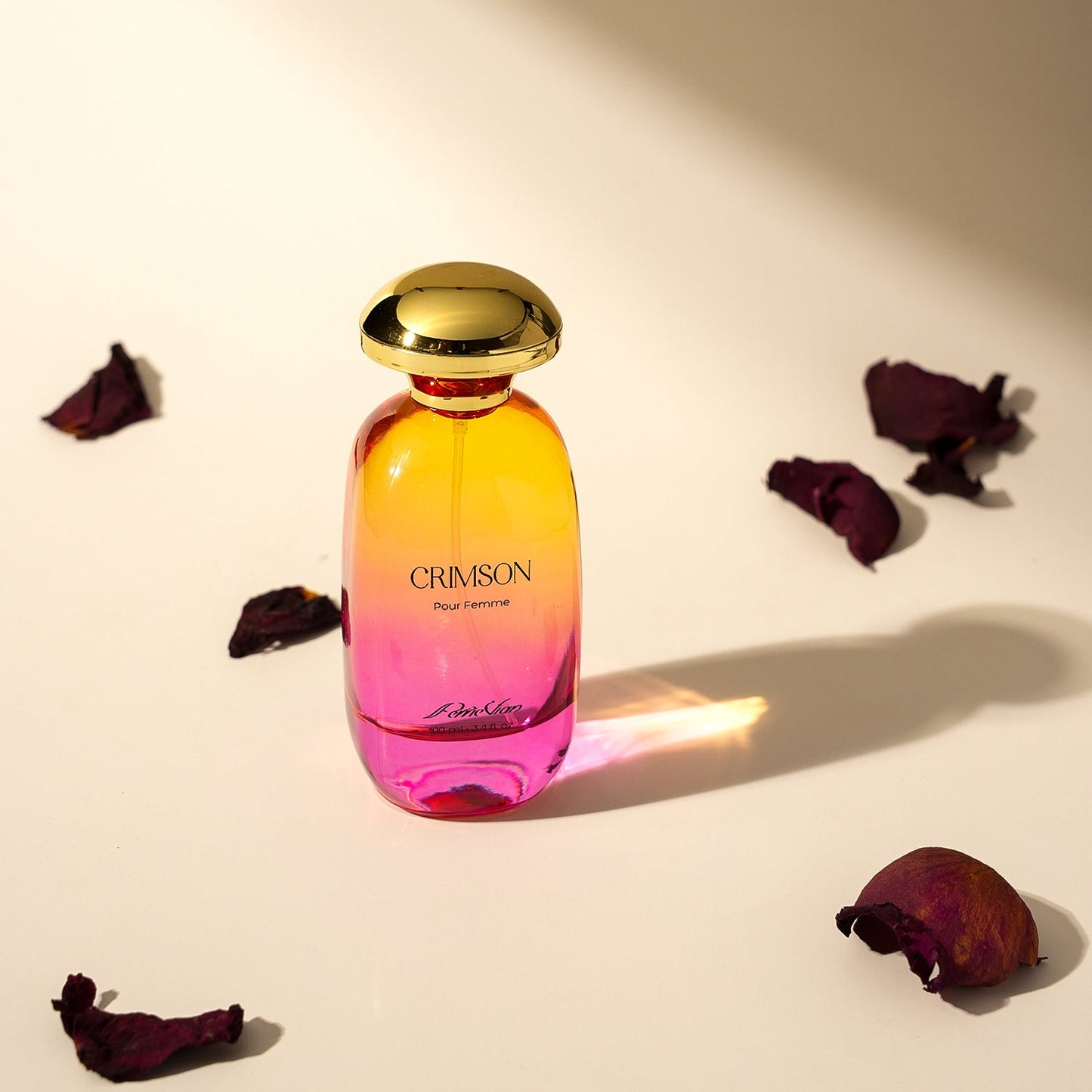 Perfume bottle labeled 'Crimson' with a gold cap on a light background with dried flowers.