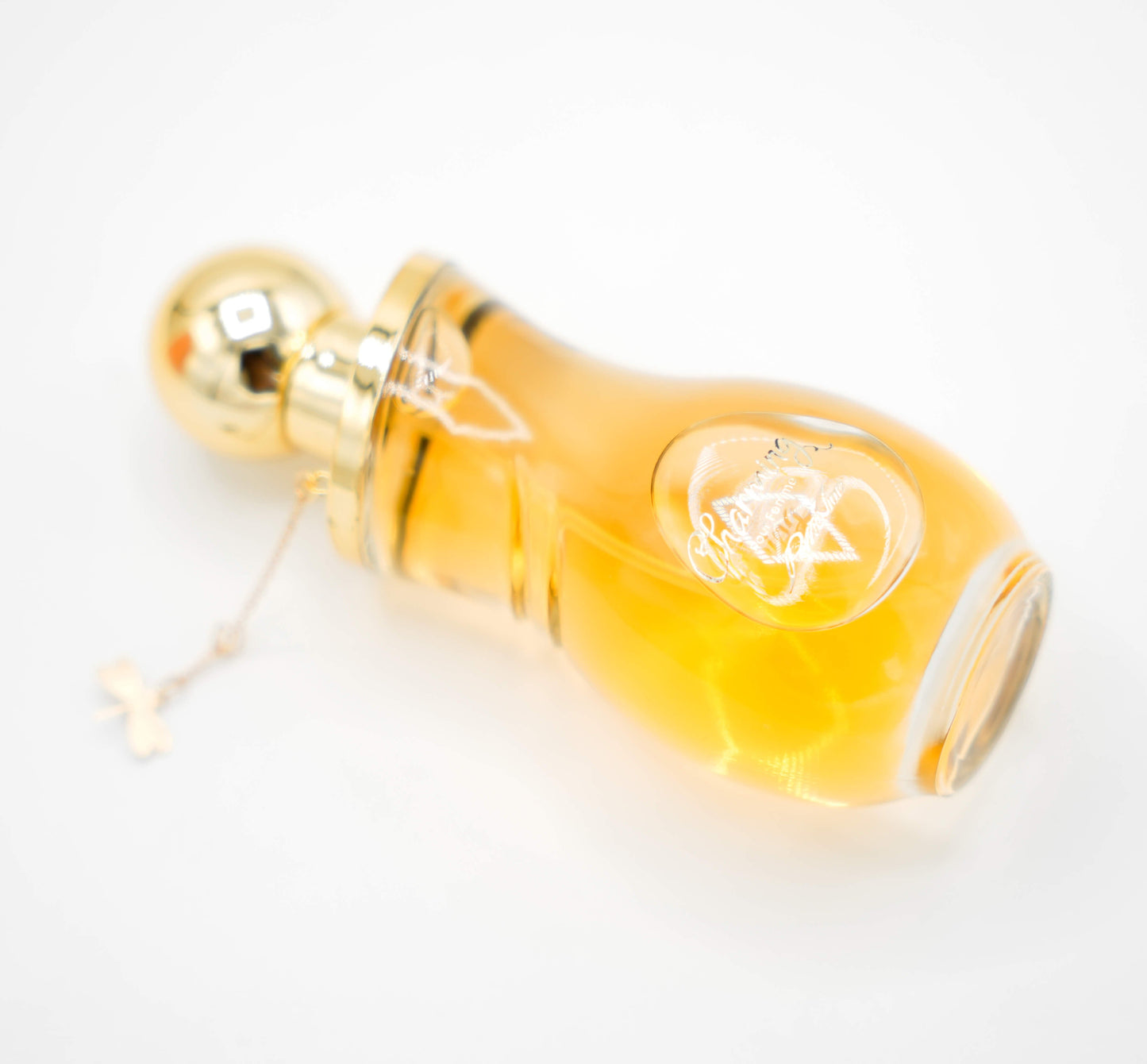 A 100ml bottle of 'CHARMING EDP' for women displayed on a white pedestal with a yellow liquid inside. The bottle has a golden cap and there is a green leaf to the top right of the image.