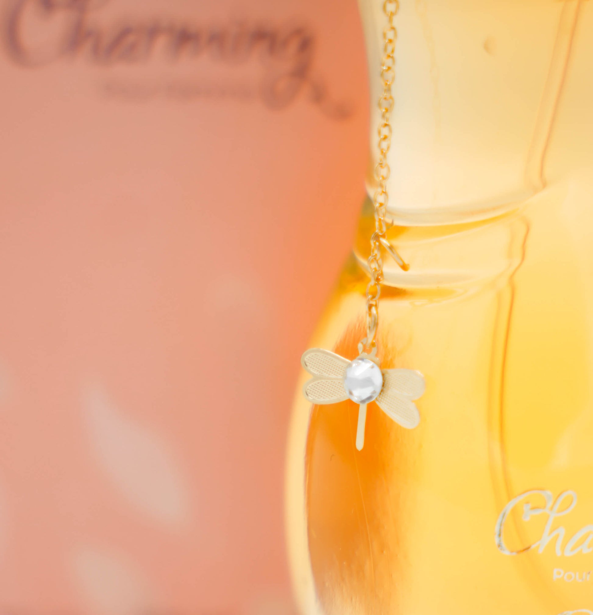 A 100ml bottle of 'CHARMING EDP' for women displayed on a white pedestal with a yellow liquid inside. The bottle has a golden cap and there is a green leaf to the top right of the image.