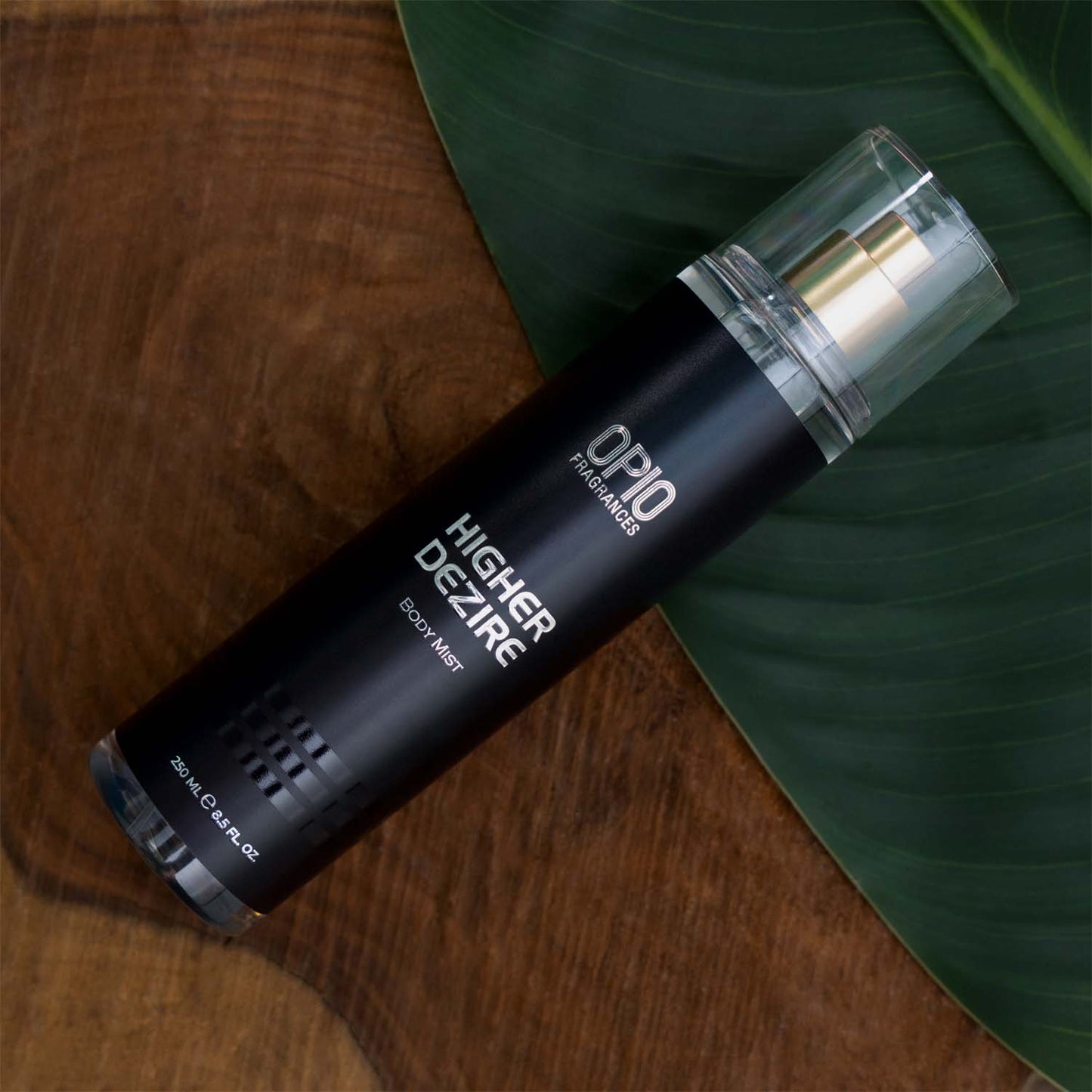 A bottle of 'HIGHER DEZIRE BODY MIST (For Men)' body mist placed on a wooden surface with a green leaf in the background.