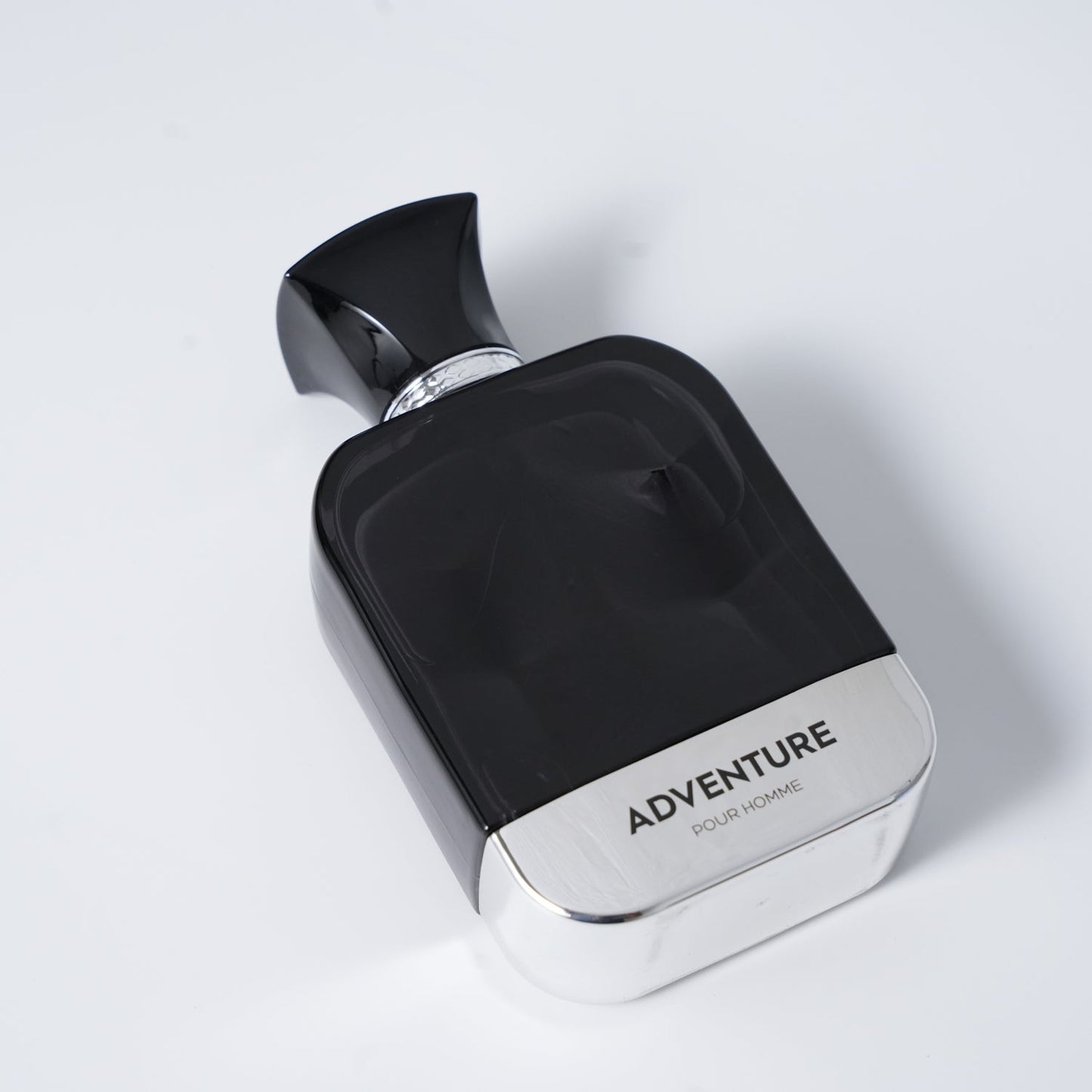 A sleek black perfume bottle labeled "ADVENTURE POUR HOMME" with a silver base and ornate cap, set against a light gray background.