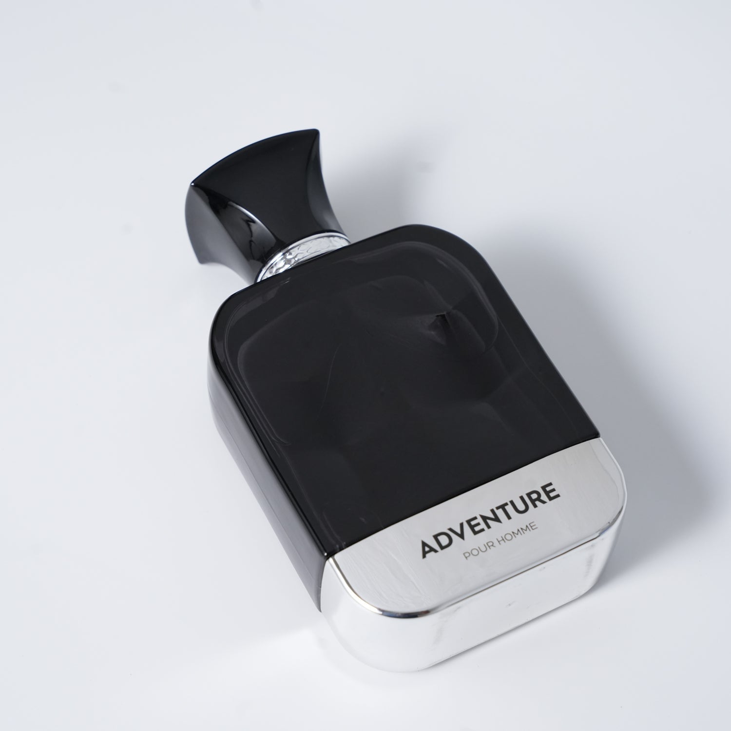 A sleek black perfume bottle labeled "ADVENTURE POUR HOMME" with a silver base and ornate cap, set against a light gray background.