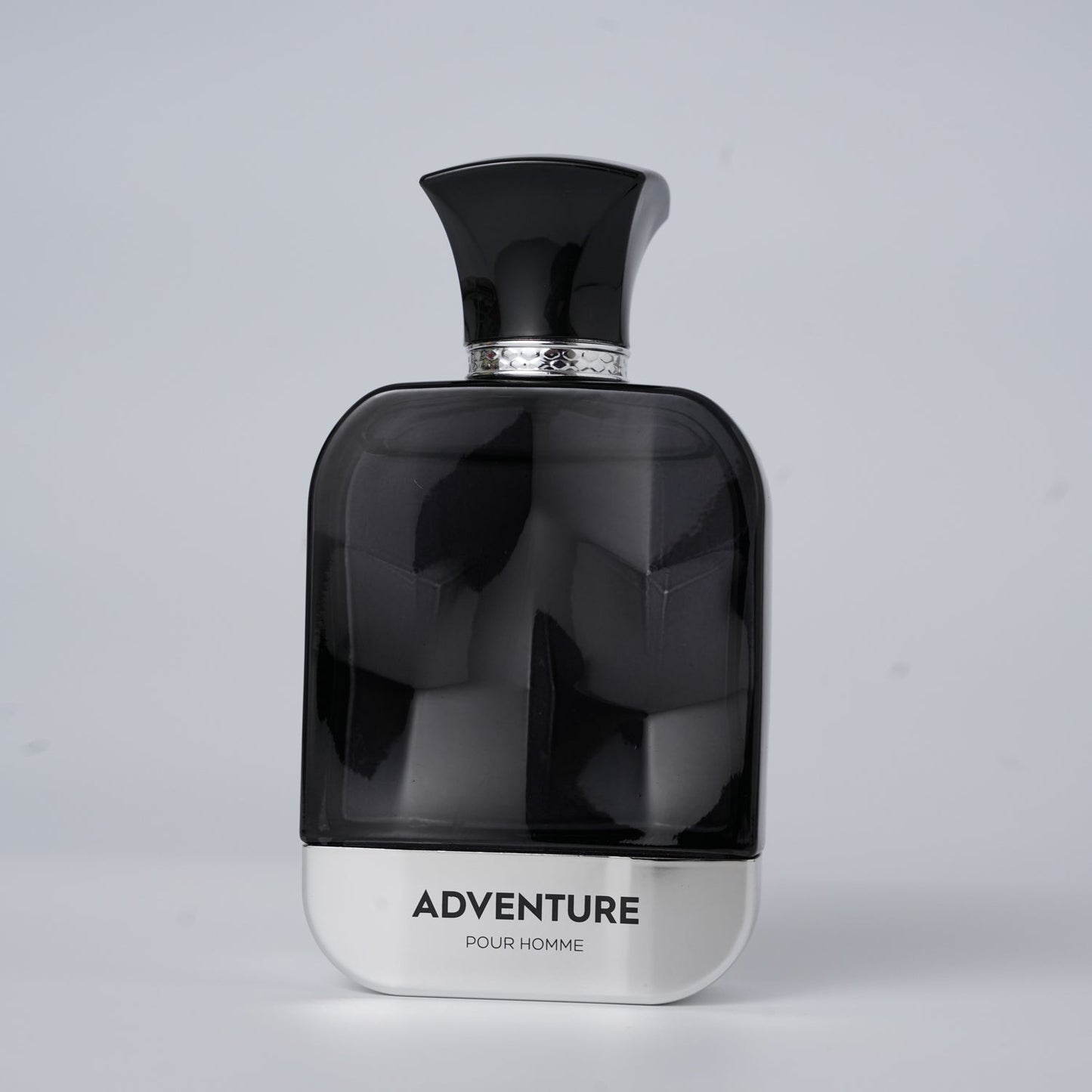 A sleek black perfume bottle labeled "ADVENTURE POUR HOMME" with a silver base and ornate cap, set against a light gray background.