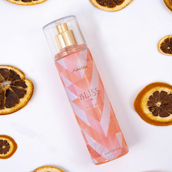 A bottle of 'Bliss' body mist for women, with a clear liquid visible inside the bottle. The bottle is placed on a surface with several sliced oranges and whole oranges in the background.