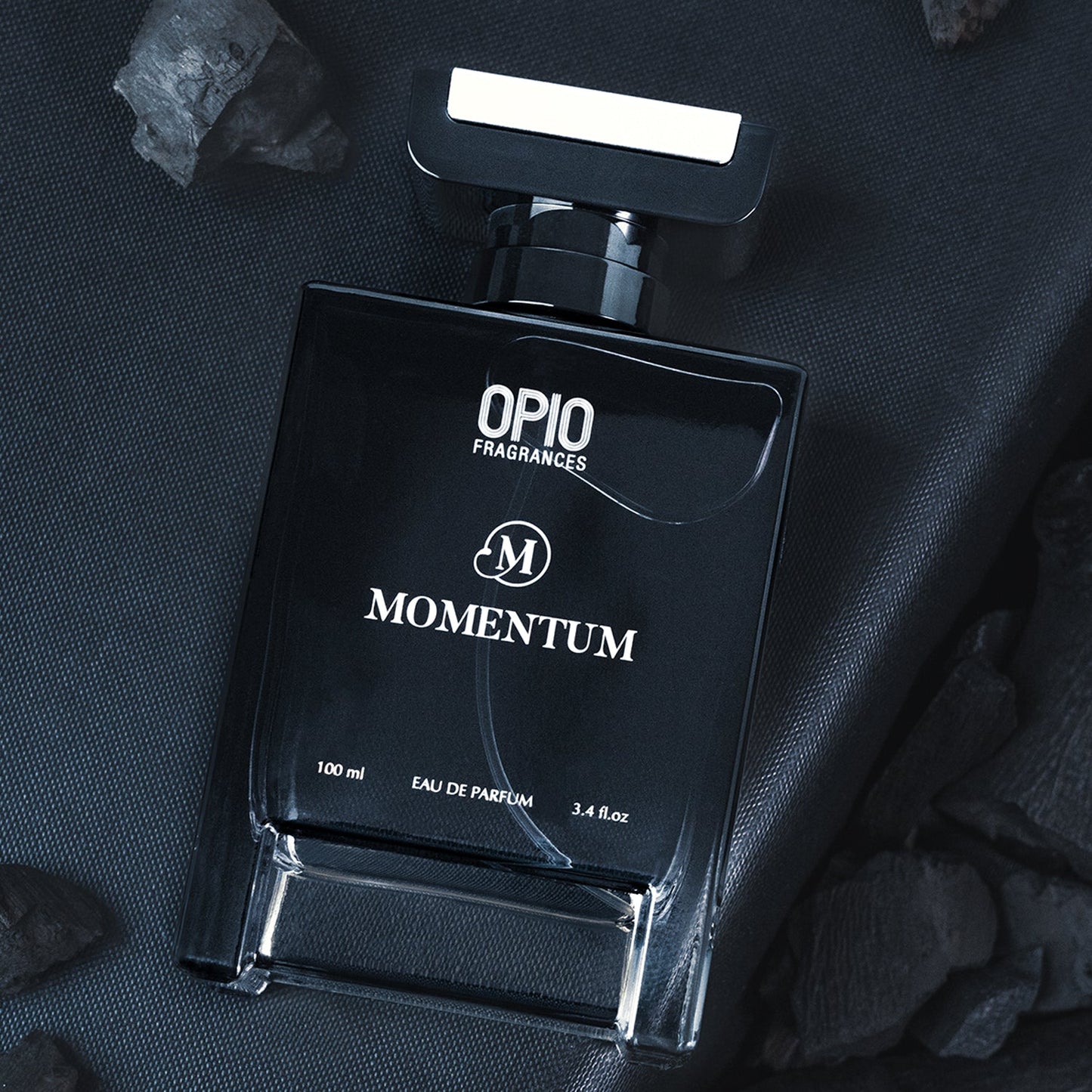 A black bottle of OPIO Momentum eau de parfum for men, with a clear label and a silver cap, displayed on a dark textured surface.