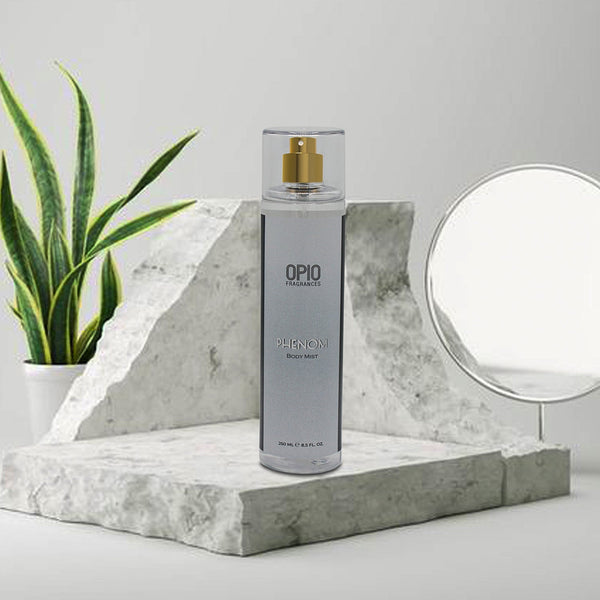 A sleek bottle of OPIO Phenom Body Mist stands on a marble display, complemented by a plant and a mirror in a minimalist setting.