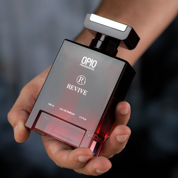 A man's hand holding a bottle of OPIO Revive fragrance for men.