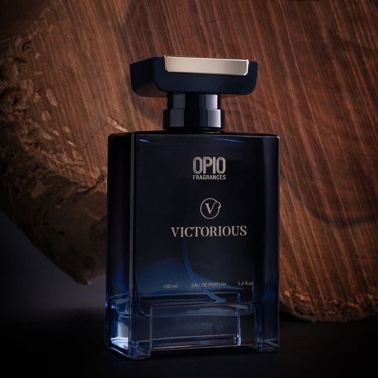A clear glass bottle of OPIO Victorious fragrance for men, with a blue label and a metallic cap, displayed in front of a wooden background.